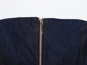 Détail macro du tissu denim bleu foncé avec coutures orange et fermeture éclair dorée