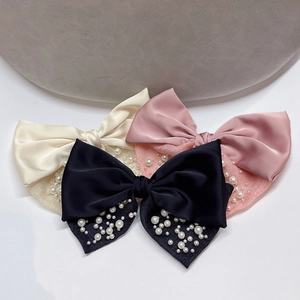 Dettaglio di tre fermagli per capelli a fiocco in raso crema, rosa e nero con perle