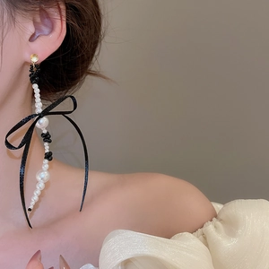 Detail of long drop earrings featuring black silk ribbon bows and white gradient pearls