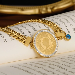 Golden stainless steel coin bracelet with white crystals and devil eye charm on a book