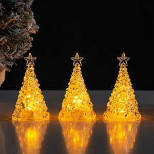 Three glowing crystal mini Christmas tree lights with warm yellow LED on dark surface