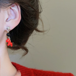 Detail view of red pony earring with star stud and black bead on a real model