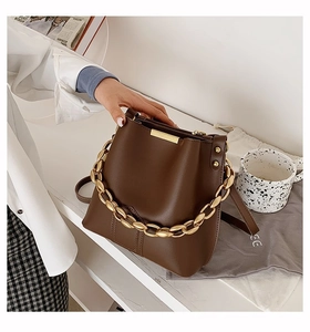 Detail of dark brown bucket bag featuring thick matte gold chain handle and fine texture