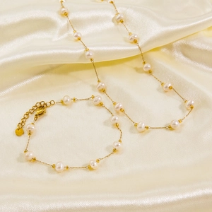 Elegant gold titanium steel jewelry set featuring natural pearls on a soft silk background