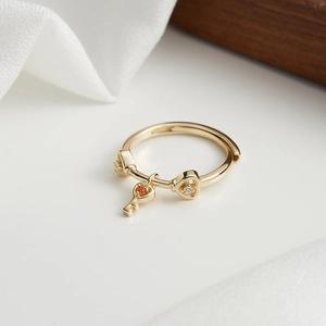 Dettaglio macro di anello in argento dorato con ciondoli a cuore e chiave e cristalli