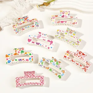Macro detail of eight cream hair claws with diverse heart prints and 'LOVE' patterns