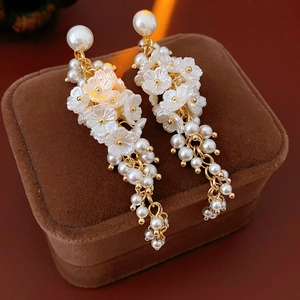 Detail of white resin flower earrings with pearls on a brown velvet jewelry box