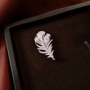 Macro detail of 18k gold-plated feather brooch with zircon stones and brushed texture