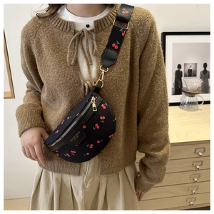 Close-up of black crossbody bag featuring red cherry prints and golden hardware