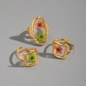 Detailed shot of gold hammered rings featuring resin-set real orange and green dried flowers