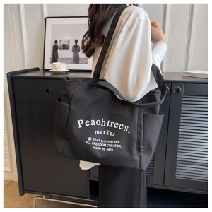 Detail of a large black canvas tote bag with white lettering and side pockets on model