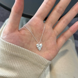Minimalist S925 sterling silver heart necklace held by hand over a beige knit sweater