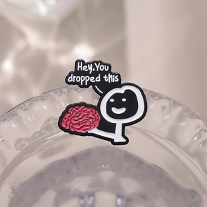 Funny metal badge with stick figure holding a pink brain and 'Hey. You dropped this' text