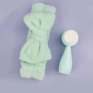 Flat lay of mint green bow headband and soft bristle facial cleansing brush set