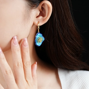 Detailed view of vintage blue flower enamel earrings with gold accents on a model