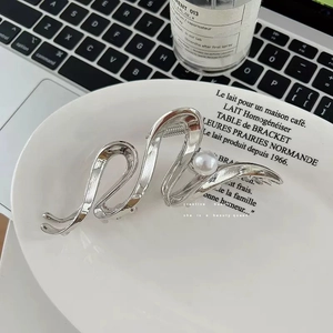 Detail showing wavy silver metal hair claw clip with pearl on white ceramic plate