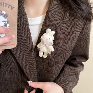 Cute beige knitted rabbit brooch with pink scarf pinned on a brown wool coat detail