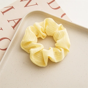 Close-up of yellow chiffon daisy scrunchie with soft pleats on a textured ceramic tray