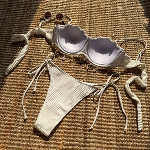 Flat lay of white ribbed bikini with starfish charms on a rustic woven straw mat