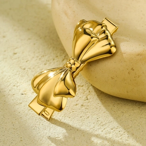 Elegant gold metal bow hair clip with a polished finish on a natural stone surface