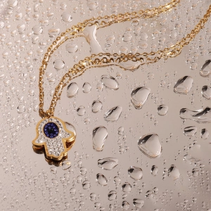 Macro detail of Hamsa Hand pendant with blue stone and crystals on water drop background