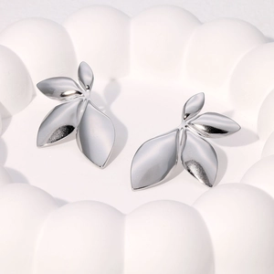 Close-up of silver leaf-shaped stainless steel earrings on a white textured tray