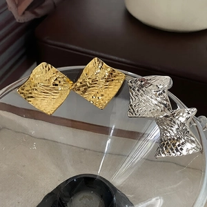 Detail of gold and silver square stud earrings with woven texture on glass bowl