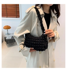 Detail of black bubble textured fabric on a stylish shoulder bag worn with a beige coat