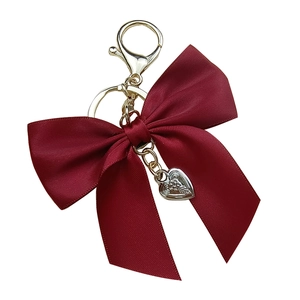 Red ribbon bow keychain with gold lobster clasp and embossed silver heart pendant on white background
