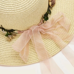 Detail of straw hat with lavender fabric flowers and a soft pink chiffon bow accent