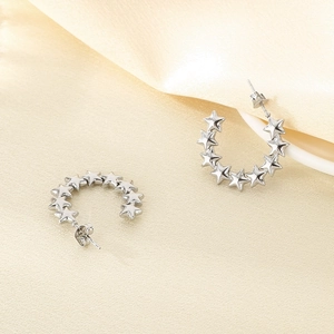 Detailed close-up of silver star earrings on beige silk fabric with soft lighting