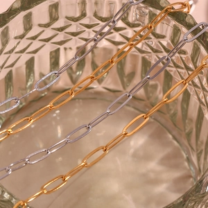 Macro shot of 18K gold and silver paperclip chain links on a textured glass surface