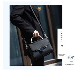 Detail of black pebbled leather handbag with gold metal handle and round lock buckle