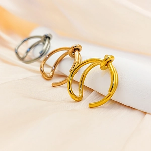Three minimalist knotted ear cuffs in gold, rose gold, and silver on silk fabric