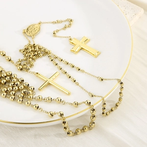 Detailed view of a golden rosary necklace with cross pendants on a white porcelain dish