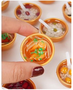 Macro detail of miniature golden bowl keychain showing realistic resin noodle soup and shrimp