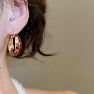 Detail of model wearing vintage gold and dark red enamel crossover huggie hoop earrings