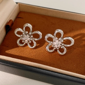 Macro shot of silver hollow flower stud earrings with zircon inlay on dark velvet