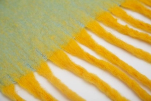 Close-up of yellow and light green textured scarf with thick soft tassels and knit detail