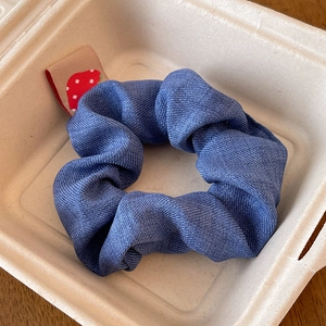 Detailed shot of a denim blue scrunchie with a cute red strawberry tag in a paper tray
