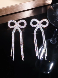 Detail of bowknot tassel earrings with sparkling rhinestones on a black background