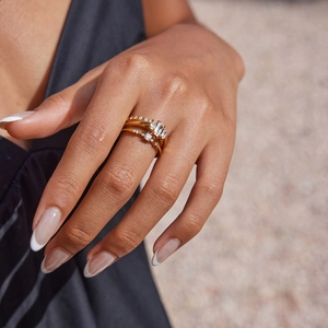 Close-up of stacked gold rings with zircon stones on a model's hand in sunlight