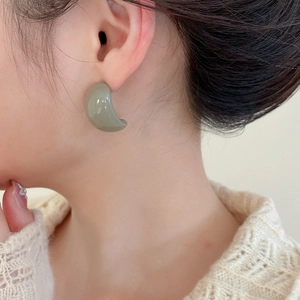 Close-up of olive green acrylic C-shaped stud earrings worn by a model with knitwear