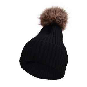 Dettaglio di un cappello in maglia a coste nere con un grande pompon di pelliccia marrone