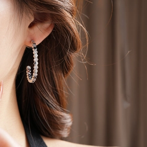 Vue macro d'une boucle d'oreille hexagonale en C argentée avec zircons sur un mannequin