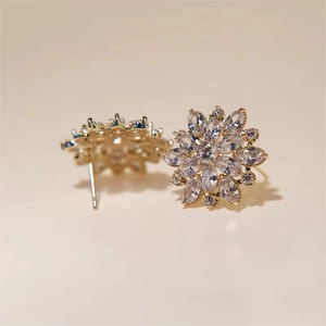 Elegant gold snowflake stud earrings with sparkling clear zircon crystals on beige background