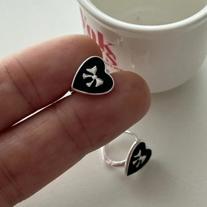 Close-up of a silver bow heart earring with black enamel finish held in hand