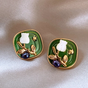 Detailed shot of green floral earrings with gold foil and pearls on beige silk