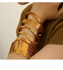 Detail of layered gold bangles featuring feather design and various textures on arm