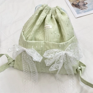 Detail of light green drawstring backpack with white lace bows and textured fabric